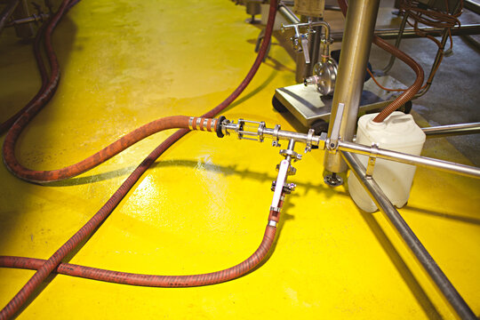 pipes and hoses connected to beer vats on a yellow floor of a microbrewery