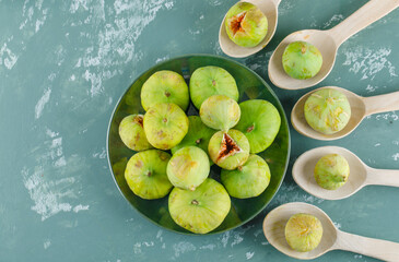 Green figs in wooden spoons and plate on a plaster background. flat lay.