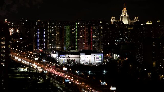 A night view from above to Moscow city. An active traffic on the avenue and many cars, running between buildings, a lot of colored lights, skyscrapers with glowing windows. Tilt up effect. 4K. 60 fps
