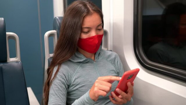 Face mask concept. Woman wearing mandatory mask in public transportation. Train transport commuter. Multiracial woman passenger using mobile smart phone with face covering on commute