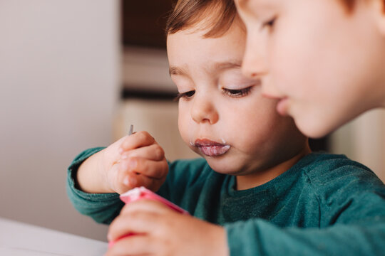 Young boy helping his little brother to eat a strawberry yoghurt.