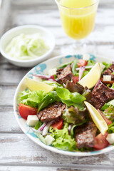 Tasty Salad with Grilled Beef Pieces, Cherry Tomatoes, feta Cheese and Kalamata Olives. Bright wooden background. Close up.