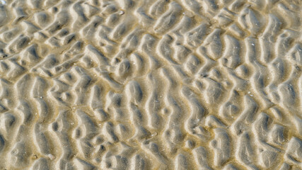 Aerial top view of clear water and patterned sand as the tide comes in at the beach.