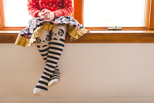 Young child sitting on window wearing cute tights