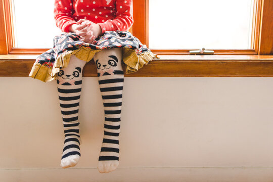 Young child sitting on window wearing cute tights