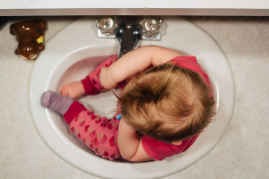 Toddler girl sitting in sink while brushing teeth