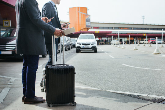 Black and Caucasian Businessmen Using Cellphones as They Wait For Taxi