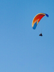Paraglider flying in blue sky.
