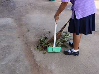 Female students sweeping the leaves on the concrete floor.