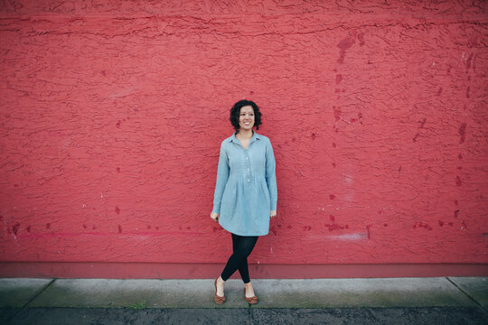 Young happy woman standing near pink red wall outside