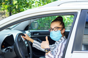 beautiful successful smiling rich business woman in medical protective mask sitting in gray car, wearing glasses showing thumbs up super, prosperous business lady style Lady is driving a car for work