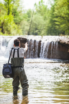 Young Man with Equipment Box Fishing near a Waterfall