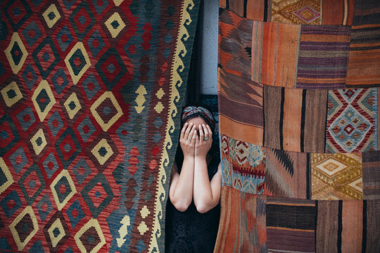 Woman covering her face with hands in front of a colorful patchwork