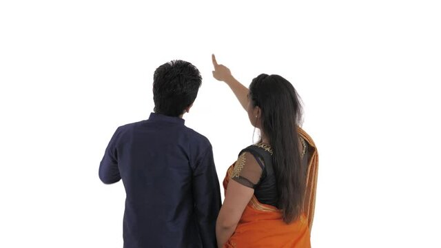 Back view of Indian couple. Woman pointing finger into distance and nodding head. Man confused scratching nape of the neck with left hand. Choosing right way. Isolated on white background