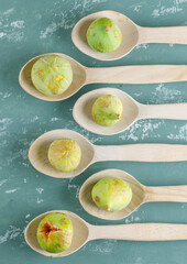 Green figs in wooden spoons on plaster background, flat lay.