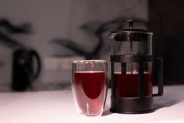 French press and tea in double-bottom glass on white table.