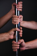 Four hands holding a pole dance bar. Dark background.