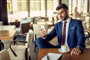 Pensive businessman reading text message on smart phone in a cafe,