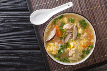 Fragrant Japanese thick rice soup Zosui with egg, mushrooms, vegetables close-up in a bowl on the table. Horizontal top view from above