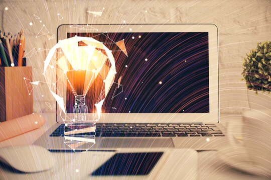 Computer on desktop in office with bulb icon hologram. Double exposure. Concept of idea.