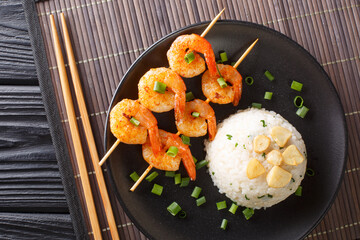 Delicious Japanese garlic fried rice served with shrimp kebabs close-up in a plate on the table. horizontal top view from above