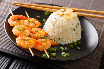Asian garlic fried rice served with shrimps on skewers close-up in a plate on the table. horizontal