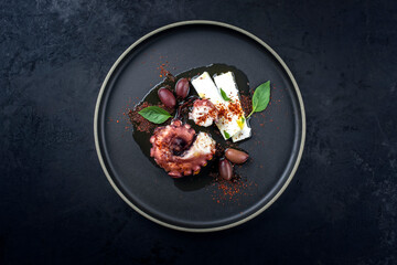 Modern Style traditionaler griechischer Chtapodi Scharas mit gegrillten Oktopus, Oliven und Feta Käse angeboten als Draufsicht auf einem Nordic Design Teller mit Textfreiraum