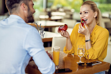 Happy woman eating donuts and talking to her boyfriend in a cafe.