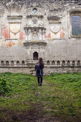 Fototapeta na wymiar Autumn trip, travel, vacation, weekend: young woman, tourist with a backpack and warm coat stands in dilapidated old synagogue. Back view. Rashkov, Moldova. Selective focus.