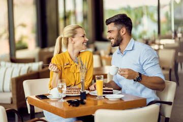 Happy couple talking while eating cake and drinking coffee in a cafe.