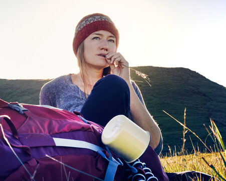 Female hiker with her back pack taking a break in a field surrounded by mountains.