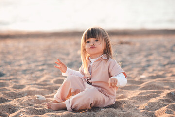 Cute baby girl 1-2 year old sitting on sand at beach over sea background close up. Looking at camera. Childhood. Summer season. Happiness.