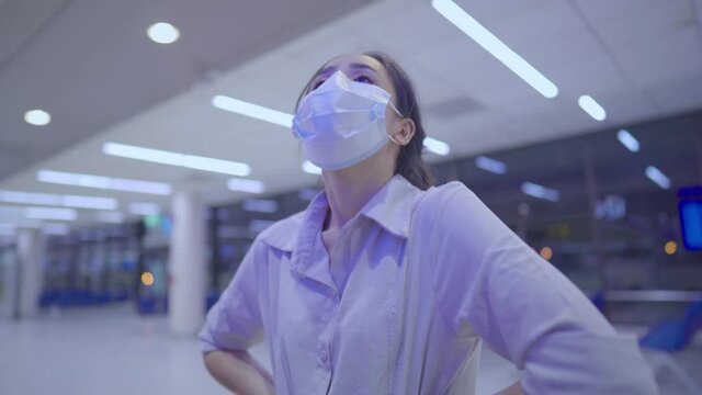 Young woman wear face mask looking at flight time screen, inside empty airport terminal, Risk of travel during covid-19 pandemic, new normal social distancing, Transmit disease prevention, front vieW