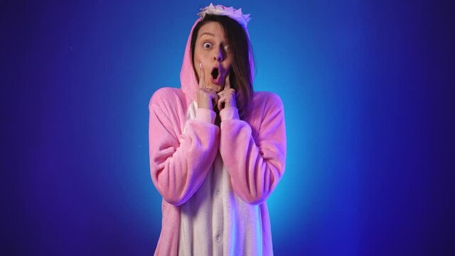 Positive girl in pink pajamas burst puffy cheeks with her palms