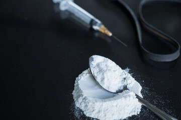 Morphine in syringe and powder morphine on spoon with black rubber band on black wood background. Illegal drug. addictive substance, narcotic, habit-forming substance concept.