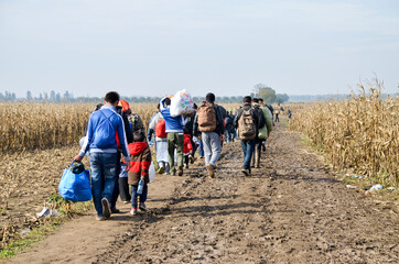 Refugees and migrants walking on fields. Group of refugees from Syria, Iraq and Afghanistan on their way to European union. Balkan route. People walking  - obrazy, fototapety, plakaty