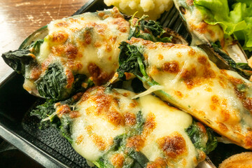 Closeup of baked New Zealand mussel with cheese and spinach on black plate served with smashed potato.