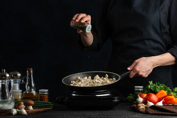 The professional chef peppers frying meat in the pan at restaurant kitchen on dark blue background....