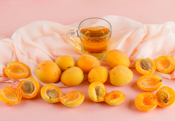 Apricots with tea on pink and textile background, high angle view.