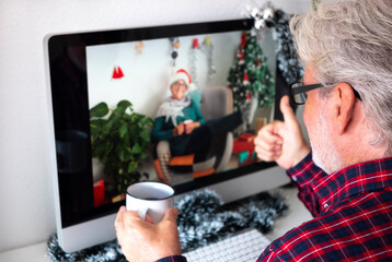 A bearded senior man on video call for Christmas greetings with a female friend, smiling happily relaxing at home with a coffee mug