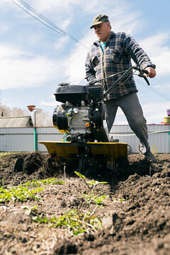 Senior man in cap walking with cultivating machine in sunlight
