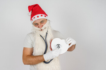 Fototapeta na wymiar Santa Claus with a stethoscope checks the heartbeat of a gift - a heart. Isolated background.