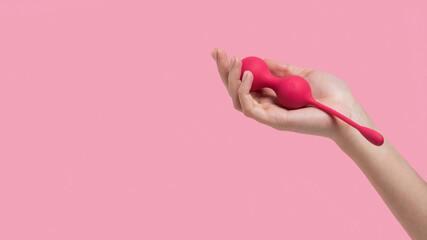 Female hand holding sex toys on a pink background. Kegel balls Geisha balls. Pink vaginal balls in a woman hand. Sex toys for girls. Place for text. Sex shop concept. Copy space. Adult store.