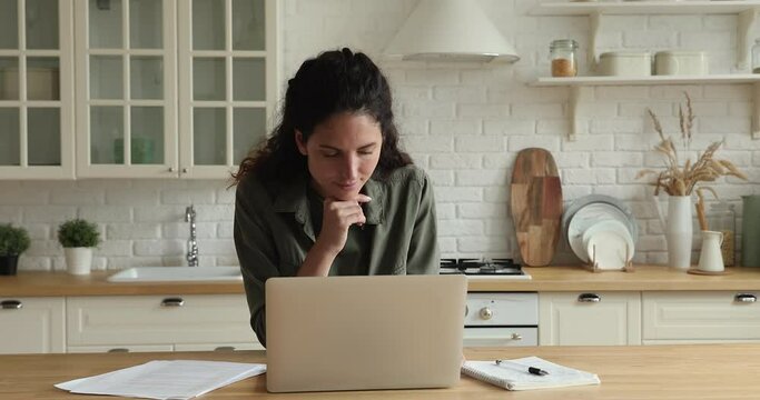 Attractive caucasian business woman entrepreneur do telecommute work from home standing in domestic cozy modern kitchen think over task using laptop device, application and internet 5g fast connection