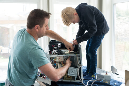 Father and Son Repairing Broken Microwave Oven Appliance At Home In Kitchen