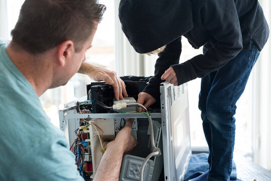 Father and Son Repairing Broken Microwave Oven Appliance In Kitchen