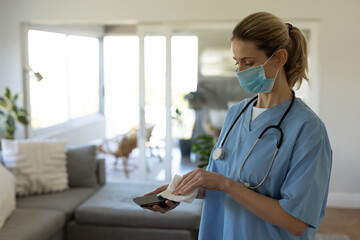 Female health worker wearing face mask wiping her smartphone with tissue