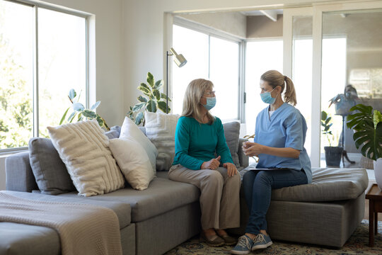 Female Health Worker And Senior Woman Wearing Face Masks Talking At Home