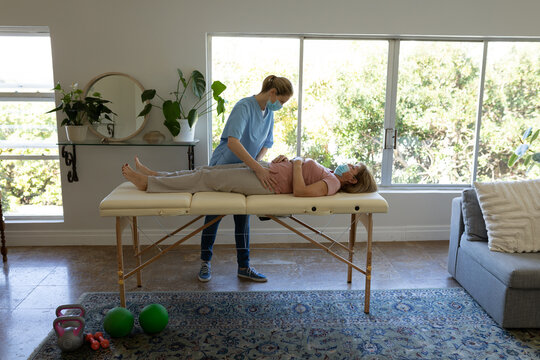 Female health worker stretching hips of senior woman at home
