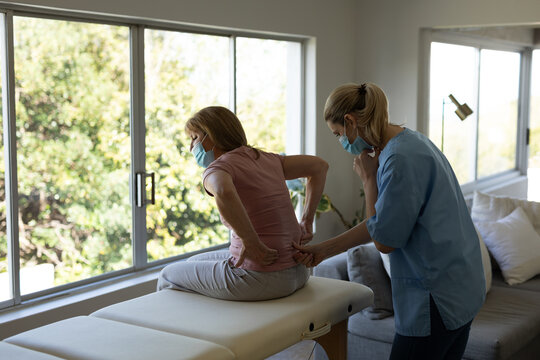Female health worker stretching back of senior woman at home
